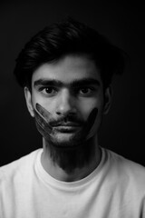 Young Indian man having a black hand print painted on face looking at camera. gender fluid lgbt identity racial equality concept. Racism concept portrait. Face painting on male face.