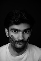 Young Indian man having a black hand print painted on face looking at camera. gender fluid lgbt identity racial equality concept. Racism concept portrait. Face painting on male face.