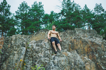 A young man with abs cubes on the background of the forest. Athletic pumped-up man on a rock background.