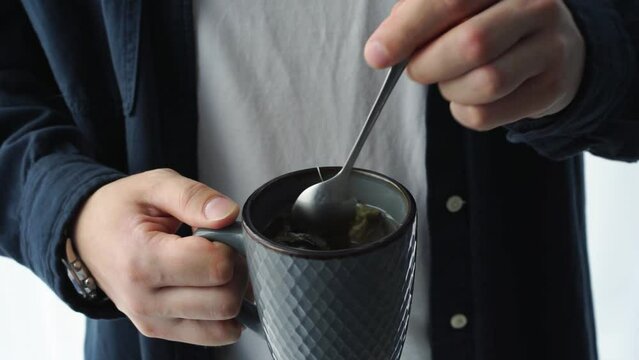 a man holds a cup of tea in his hands.
Man stirs tea with a teaspoon