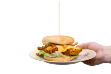 A burger with a crispy breaded piece of chicken breast on iceberg lettuce, topped with a piece of cheddar cheese, covered with crispy fried bacon and juicy sauce is served on a plate by a man's hand.