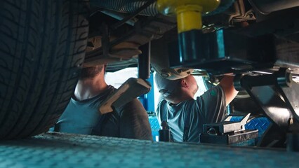 Auto technicians collaborate under a hoisted vehicle, expertly maneuvering equipment in a well-lit repair bay.