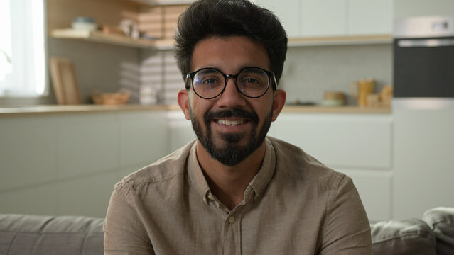 Portrait smiling Arabian Indian muslim middle eastern man happy millennial guy homeowner alone on couch relax on sofa in kitchen male renter own estate apartment looking at camera toothy smile at home