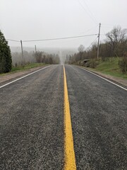 A country road leading down a large hill to a rural foggy Forested Area