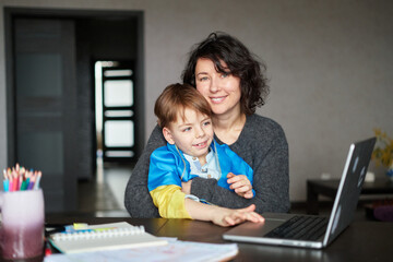 Ukrainian mother and son with flag sitting with laptop at home studying .Happy smiling family hugs...