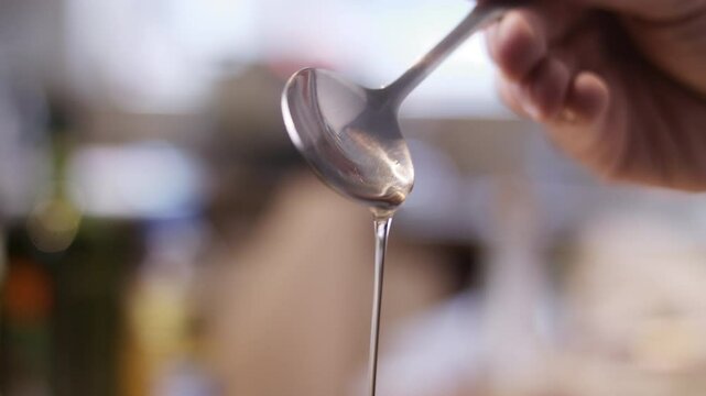 Closeup slow-motion of hand dropping cooking oil from spoon against blur background