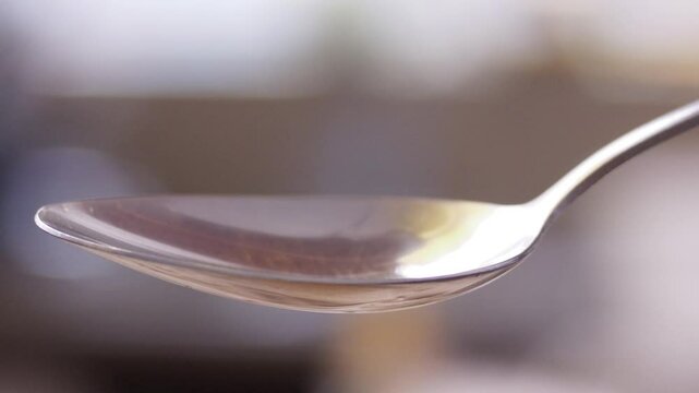 Closeup slow-motion of oil dropping on a spoon against blur background
