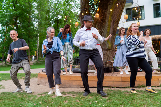 Cheerful dance party outdoors, featuring individuals of different ages enjoying the festive ambiance under illuminated string lights. They are dancing swing dance in summer city park