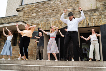 Cheerful dance party outdoors, featuring individuals of different ages enjoying the festive ambiance under illuminated string lights. They are dancing Lindy Hop dance on the city theater stairs.