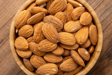 Overhead view of a bowl full of peeled almonds on a wooden surface