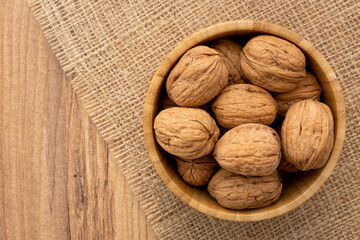 Overhead view of a wooden bowl full of shelled walnuts on a piece of burlap