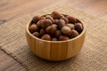 A wooden bowl full of shelled hazelnuts on a piece of burlap
