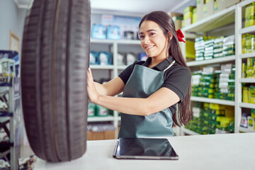 cheerful latina saleswoman holding and checking new tire at the counter in a small auto parts supply store	