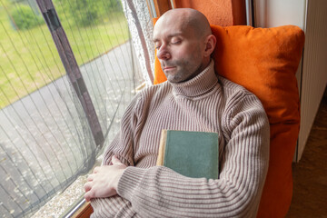 Young man relaxing with book on windowsill in old house, reclining on windowsill, self-reflection,...