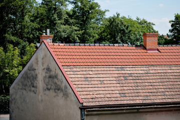 House Roof With Fresh And Old Red Tiles and Brick Chimneys Surrounded by Lush Green Trees