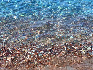 Clear sea water with colorful pebbles on the beach.