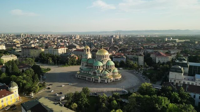 Aerial drone view of St. Alexander Nevsky Cathedral in the Sofia city, Bulgaria. Footage of the iconic Bulgarian orthodox church during sunrise surrounded by green trees. 