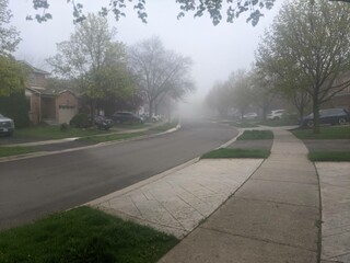 A Suburban Street in the spring on a foggy day with sidewalks, houses and a road