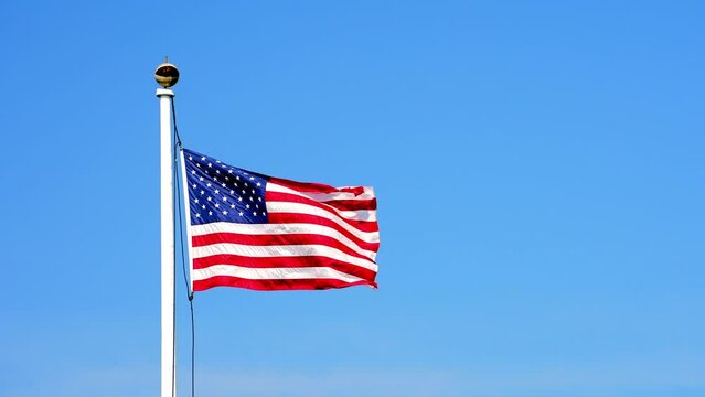 American flag waving proudly in the wind against a backdrop of a clear blue sky in slow motion