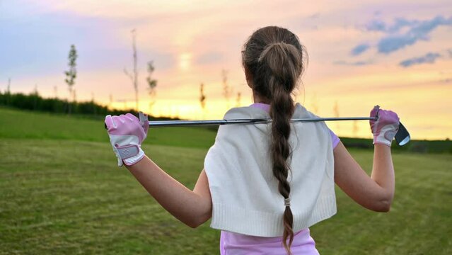 Woman holding a golf club on her shoulders, watching the sunset