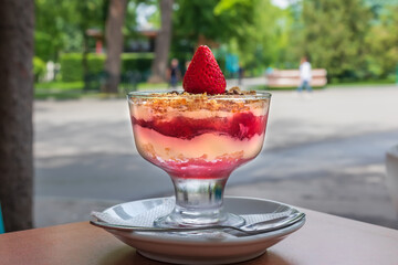 Ice cream with yogurt, jam and strawberries in a glass on the table, summer outdoor cafe area. Dessert close up