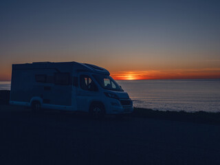 Silhouette of a camper van parked on the side of a road near the ocean. The sky is a beautiful mix...