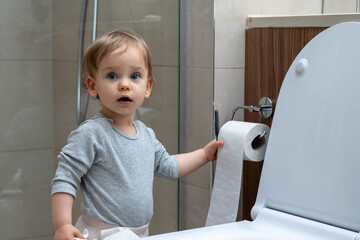 Toddler ripping up toilet paper in bathroom. Concept of naughty baby