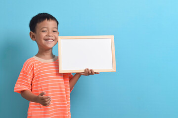 Cute little Asian boy holding a blank board isolated on blue background. Space for text, copy...