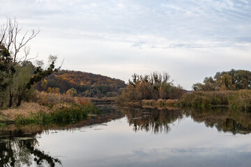 Siverskyi Donets river shore in Ukraine with autumn trees and cloudy sky reflections
