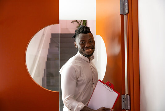 Confident young businessman with clipboard by office door