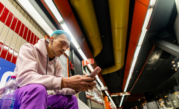 Young man with blue hair using smartphone at subway station