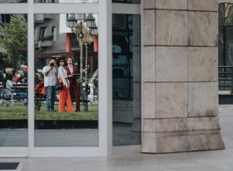 Reflection of two friends posing and taking pictures in an urban cityscape, capturing a candid and artistic moment in a bustling environment.
