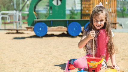 Сute little girl on playground in sandpit. Child playing with sand molds and making mud pies. Outdoor creative activities for kids