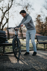 Obraz premium A young man pauses his bike ride to enjoy the tranquility of the park as the sun sets, providing a peaceful escape.