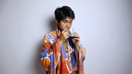 Young Asian man wearing a blanket is enjoying a cup of coffee