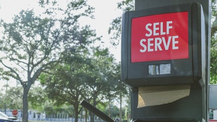 Vibrant Self-Serve Gas Station Sign Surrounded by Lush Green Trees in a Serene Natural Setting