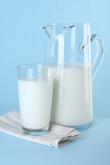 Jug and glass of fresh milk on light blue background