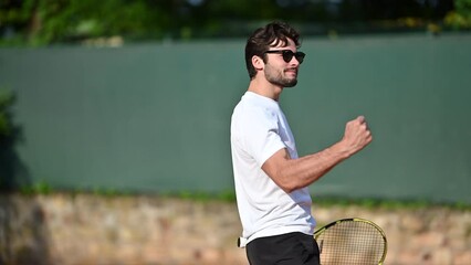 A young handsome male Caucasian tennis player, happy winning, celebrates a victory after winning a match on an outdoor court. Successful professional athlete winning championship and showing his joy.