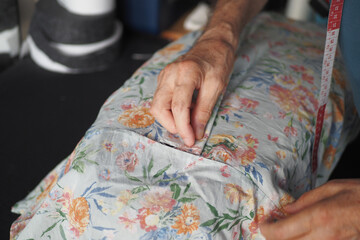 Tailor sewing fabric with measuring tape, showing precision and craftsmanship in closeup shot