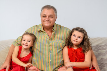 Portrait of a senior grandfather with his granddaughters on the sofa