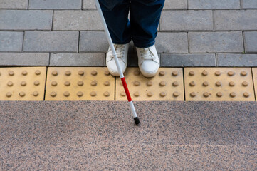 Close-up of female foot, walking stick and tactile tiles.