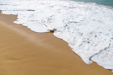 Waves crash on sandy beach under sunny sky, creating beautiful scene