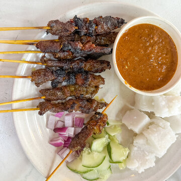 Top view of satay (sate), a popular Malaysian street food.  Served together with peanut sauce, sliced cucumber, onion and rice cube (nasi impit).