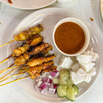 Top view of satay (sate), a popular Malaysian street food.  Served together with peanut sauce, sliced cucumber, onion and rice cube (nasi impit).