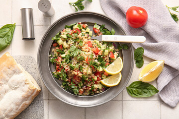 Plate with delicious tabbouleh salad and bread on light tile background