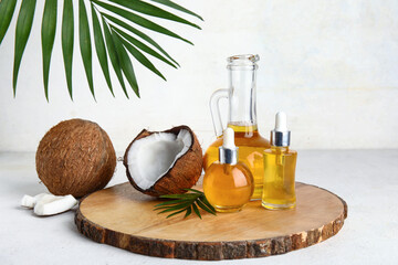 Wooden stand with bottles and decanter of coconut cosmetic oil on white background