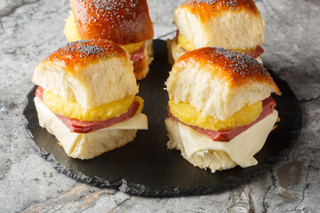 Baked Hawaiian sliders with ham, cheese, pineapple feature mini rolls with a savory poppy seed butter sauce closeup on the slate board on the table. Horizontal