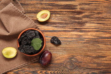 Bowl with tasty dried plums on wooden background