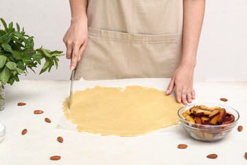 Woman preparing dough for plum galette on white table