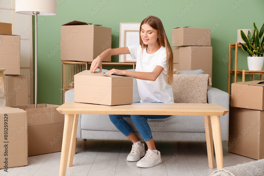 Poster Pretty young woman unpacking cardboard box in new apartment. Moving house concept